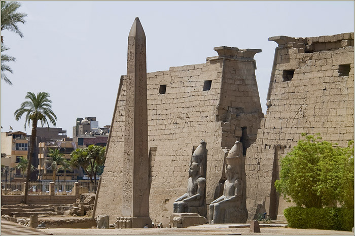 Там, где Нил прорезает Нубийское нагорье и вырывается на равнину, расположены знаменитые асуанские каменоломни. Начиная с эпохи Древнего царства, а возможно, и раньше, здесь добывали розовый гранит. Камень этот играл особую роль в жизни египтян: из него делали порталы храмов, саркофаги, статуи царей и, конечно же, массивные обелиски.  Один из таких остался незавершенным, так и не покинув пределы каменоломни. Это знаменитый Асуанский обелиск, до сих пор вызывающий интерес ученых-египтологов.  ОХОТА НА ОБЕЛИСКИ  Само слово «обелиск» греческого происхождения, и означает оно «вертел». Египтяне же называли эти каменные столбы «бен-бен». Так именовали упавший с неба камень пирамидальной формы, который установили на столбе в священной столице — городе Иуну (греки называли его Гелиополисом).  Обелиск у храма в Луксоре    Все египетские обелиски так или иначе повторяют форму священного бен-бена: это столбы правильного квадратного сечения с пирамидальной вершиной, которая обычно покрывалась золотом или медью (разумеется, металлическое покрытие до сегодняшнего дня не сохранилось). Практически все известные монументы изготовлены из розового гранита.  Любопытно, что немалое их число находится за пределами Египта. После установления своего господства римляне начали вывозить обелиски в Италию. Сегодня Вечный город украшают тринадцать каменных столбов из Египта. В XIX веке настоящую охоту за египетскими древностями устроили французы и англичане. Не обошли они своим вниманием и обелиски. Поэтому их можно увидеть и в Париже, и в Лондоне, и даже в Нью-Йорке.  ТАЙНЫ КАМЕНОТЕСОВ  Наибольшего расцвета производство обелисков достигло в период Нового царства (XVI—XI вв. до н. э.). Особенно отличились в этом отношении фараоны Тутмос III и Рамсес II. Последний, как считается, за время своего правления успел воздвигнуть целых 23 глыбы. В среднем высота обелисков равнялась 20 метрам, вес каждого превышал 200 тонн. Практически все известные на сегодня монументы обильно покрыты иероглифами, славящими царей и их деяния.  Но самый большой из известных в Египте обелисков — Асуанский. Его длина составляет 41,8 метра! Он не был завершен, на нем нет никаких надписей, поэтому до сих пор не определена дата его изготовления. Но специалисты (почему-то) относят его ко времени Древнего царства, то есть к эпохе Великих пирамид.  Предполагается, что добыча камня для обелисков производилась следующим образом. Вначале в скале вырубали отверстия, затем в них забивали деревянные клинья, которые поливали водой. Дерево разбухало и разламывало породу. Получившиеся блоки выравнивали и при необходимости шлифовали. Еще древнеримский историк Плиний Старший I в. н. э.) упоминал, что разделка камня осуществлялась при помощи тонких пил, под полотно которых постоянно подсыпали мелкодисперсный песок, служивший абразивом.  Но с Асуанским обелиском все обстоит несколько иначе. Он расположен на поверхности и лежит под небольшим углом к гранитному массиву. По всему периметру монолит окружен узкой траншеей шириной менее одного метра. Таким образом, получается, что глыба выдолблена в скале и работы велись сверху, а не с боков. Какой инструмент при этом использовался? Понятно, что о применении пил говорить здесь не приходится.    Боковые стороны обелиска и окружающей его траншеи имеют следы большого округлого инструмента. Впрочем, аналогичные следы встречаются во множестве. И похожи они, скорее, на следы от гигантской стамески. Но можно ли представить себе стамеску с рабочей кромкой в 30 сантиметров, режущей гранит, словно пластилин? На самом монолите, кстати, имеются многочисленные следы пропилов и традиционной техники колки при помощи клиньев. Но они оставлены явно в более поздние времена, и эти попытки не нанесли существенного урона монолиту — ни расколоть, ни распилить его не удалось.  ИНСТРУМЕНТ, КОТОРОГО НЕ МОЖЕТ БЫТЬ  Можно предположить, что Асуанский обелиск остался незавершенным, поскольку в ходе работ, возможно, была допущена ошибка, и монолит повредился. Действительно, верхнюю часть камня пересекает продольная трещина, нарушившая его цельность. Но причины такого «брака» не обязательно кроются в просчетах строителей. Это могло быть, к примеру, результатом землетрясения.  Интересно другое. Раз уж древние египтяне начали вырезать подобный монолит, значит, они собирались его как-то транспортировать  и устанавливать.  И тогда возникает вопрос: каким образом монолит, расположенный внутри скалы и окруженный узкой траншеей по периметру, можно было отделить от каменного массива?      Пять лет назад на территории асуанских каменоломен открыли для посещения туристов еще один участок, расположенный позади лежащего исполина. И здесь находится еще один незаконченный обелиск. Он меньше своего огромного соседа, и сохранилась от него только треть. Оставшуюся часть также не успели отделить от материнской породы, но работы продвинулись дальше.  Древние каменотесы начали процесс отделения монолита от каменного массива. И здесь мы видим ту же технологию: следы «лопатки» вгрызаются в гранит, как в пластилин. Узкая траншея, где человеку негде даже размахнуться для удара инструментом по породе, огибает обелиск со всех сторон. Возможно ли сделать такое при помощи каменных отбойников или пил? Однозначно, нет.  А ПОДНЯТЬ КАК?  И, кстати, о весе. Сегодня называют разные цифры, но чаще всего можно услышать, что вес Асуанского монолита составляет 1 200 тонн. Конечно, взвесить такого исполина никто не в состоянии, и его вес вычисляется арифметически. Хотя обелиск остался не отделенным от скалы, его размеры известны. Высота должна была бы составить 41,8 метра, а основание представляет собой квадрат со стороной в 4,2 метра. Стороны идут параллельно на всем протяжении, только в верхней части сужаются, образуя вершину.  Если принять среднюю плотность гранита за 2 600 кг на кубический метр, то легко можно вычислить вес монумента. И если не учитывать небольшое сужение у вершины, то расчетный вес Асуанского обелиска должен был бы составить примерно 1 900 тонн! Однозначно, это самый тяжелый в мире искусственный монолит.    И представьте себе: древние инженеры собирались такой монолит куда-то двигать и затем устанавливать. Конечно, Книга рекордов Гиннесса полна примеров, когда человек в одиночку сдвигал с места большегрузные автомобили, самолеты и железнодорожные вагоны. Но во всех этих случаях речь идет об огромных грузах, поставленных на колеса, и двигать их предстояло по ровной горизонтальной поверхности. Каким же образом можно было решить задачу транспортировки по неровной гористой местности цельного монолита весом почти в 1900 тонн?    НАСЛЕДНИКИ ИНОЙ ЭПОХИ  Искусство обработки гранита достигло в Древнем Египте небывалых высот. И оно вызывает не только уважение, но и изумление. Действительно, нельзя же объяснить все принципом «упорство и труд все перетрут». Дошедшие до нас образцы древнеегипетской гранитной архитектуры демонстрируют высочайший уровень технологии обработки и строительства. Причем чем дальше к истокам египетской цивилизации мы уходим, тем уровень этот выше.  Мастерство -создателей памятников Гизы так и осталось непревзойденным. Наоборот, налицо деградация, начавшаяся после эпохи Древнего царства, то есть после III тысячелетия до н. э. И в этом смысле вполне уместны и правомерны гипотезы тех исследователей, которые считают Древний Египет наследником еще более древней и более развитой цивилизации. Не исключено, что Асуанский обелиск тому свидетельство.  Андрей ЖУКОВ